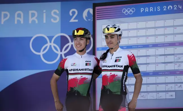 Fariba Hashimi, of Afghanistan, left, and her sister Yulduz Hashimi, pose prior to the women's road cycling event, at the 2024 Summer Olympics, Sunday, Aug. 4, 2024, in Paris, France. (AP Photo/Thibault Camus)