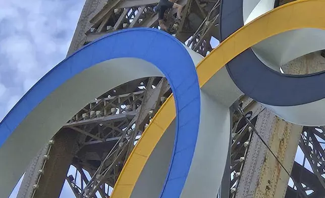 In this photo provided by Nicky Worlock, a man climbs the Eiffel Tower, during the 2024 Summer Olympics, Sunday, Aug. 11, 2024, in Paris France. (Nickey Worlock via AP)