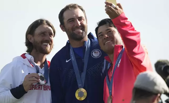 Bronze medalist Hideki Matsuyama, of Japan, right take a smart phone picture on the podium of gold medalist Scottie Scheffler, of the United States, centre, and Tommy Fleetwood, of Britain, silver medal, as they pose for the media following the medal ceremony for men's golf at the 2024 Summer Olympics, Sunday, Aug. 4, 2024, at Le Golf National in Saint-Quentin-en-Yvelines, France. (AP Photo/Matt York)