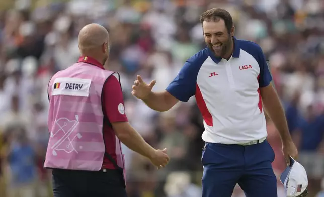 Scottie Scheffler, of the United States, smiles as he shakes hands with Thomas Detry, of Belgium's caddie after completing his round on the 18th green during the final round of the men's golf at the 2024 Summer Olympics, Sunday, Aug. 4, 2024, at Le Golf National in Saint-Quentin-en-Yvelines, France. (AP Photo/Matt York)