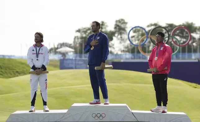 Gold medalist Scottie Scheffler, of the United States, centre, with Tommy Fleetwood, of Britain, silver medal, left, and Hideki Matsuyama, of Japan, with the bronze medal, listen to the nation anthem of the US during the medal ceremony for men's golf at the 2024 Summer Olympics, Sunday, Aug. 4, 2024, at Le Golf National in Saint-Quentin-en-Yvelines, France. (AP Photo/George Walker IV)