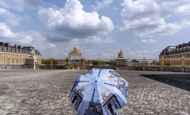 A visitor using an umbrella for shade, tours the Chateau de Versailles, whose grounds are the site of the equestrian events during the 2024 Summer Olympics, Friday, Aug. 2, 2024, in Versailles, France. (AP Photo/David Goldman)