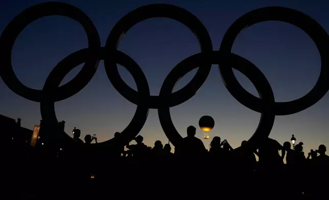 People watch the cauldron rise at sunset by the Olympic rings during the 2024 Summer Olympics, Monday, Aug. 5, 2024, in Paris, France. (AP Photo/Natacha Pisarenko)