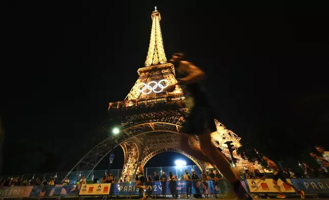 Spectators stand at the base of the Eiffel Tower as they watch runners participate in the Pour Tous marathon, at the 2024 Summer Olympics, in Paris, Saturday, Aug. 10, 2024. (AP Photo/Natacha Pisarenko)