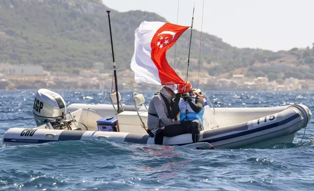 Max Maeder, of Singapore, is consoled by his coach after winning the bronze medal, at the end of competition in the men's kite final race, Friday, Aug. 9, 2024, during the 2024 Summer Olympics in Marseille, France. (AP Photo/Jacquelyn Martin)