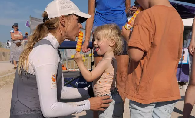 Marit Bouwmeester of the Netherlands celebrates by sharing a treat with her daughter Jessie Mae after competing in ILCA 6 dinghy class racing during the 2024 Summer Olympics, Monday, Aug. 5, 2024, in Marseille, France. (AP Photo/Carolyn Kaster)