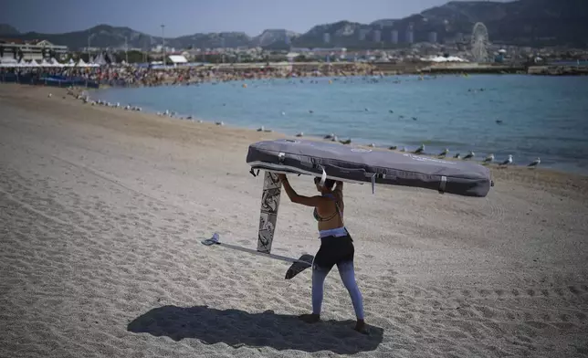 Marta Maggetti of Italy carries her windsurf board after the women's windsurfing medal race was postponed until Saturday due to lack of wind during the 2024 Summer Olympics, Friday, Aug. 2, 2024, in Marseille, France. (AP Photo/Daniel Cole)