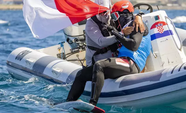 Max Maeder, of Singapore, is consoled by his coach after winning the bronze medal at the end of the competition in the final race of men's kite, Friday, Aug. 9, 2024, during the 2024 Summer Olympics in Marseille, France. (AP Photo/Jacquelyn Martin)