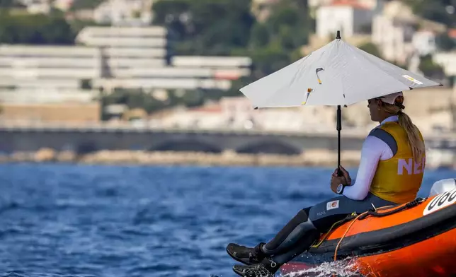 Marit Bouwmeester of the Netherlands shelters against the sun with an umbrella as she waits with others for the start of the ILCA 6 dinghy class final race during the 2024 Summer Olympics, Tuesday, Aug. 6, 2024, in Marseille, France. (AP Photo/Jacquelyn Martin)