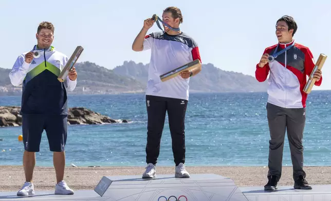 Toni Vodisek, of Slovenia, left, with silver, an enthusiastic Valentin Bontus, of Austria, with gold, and Max Maeder, of Singapore, with bronze, hold up their medals during the Olympic medal ceremony for the men's kite, Friday, Aug. 9, 2024, during the 2024 Summer Olympics in Marseille, France. (AP Photo/Jacquelyn Martin)