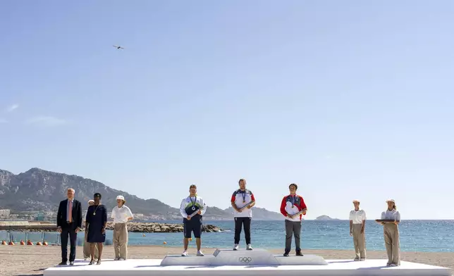 Toni Vodisek, of Slovenia, center left, with silver, Valentin Bontus, of Austria, with gold, and Max Maeder, of Singapore, with bronze, attend the Olympic medal ceremony for the men's kite, Friday, Aug. 9, 2024, during the 2024 Summer Olympics in Marseille, France. (AP Photo/Jacquelyn Martin)