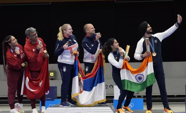 R to L, India's Sarabjot Singh uses his phone to take a selfie with teammate Manu Bhaker, Serbia's Damir Mikec and Zorana Arunovic, and Turkey's Yususf Dikec and Savval Ilayda Tarhan after the medal ceremony of the 10m air pistol mixed team event at the 2024 Summer Olympics, Tuesday, July 30, 2024, in Chateauroux, France. Serbia won the gold medal, while Turkey and India won the silver and the bronze respectively. (AP Photo/Manish Swarup)