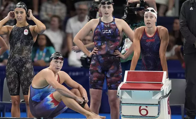 Katie Ledecky, of United States, sits on the pool deck with teammates during the women's 4x200-meter freestyle relay final at the 2024 Summer Olympics, Thursday, Aug. 1, 2024, in Nanterre, France. (AP Photo/Matthias Schrader)