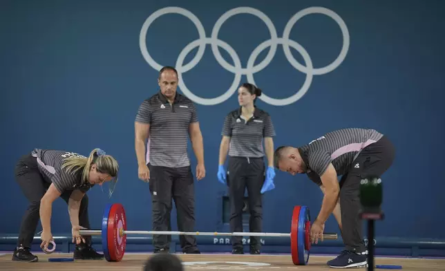 Loaders set the weight on the bar during the women's 59kg weightlifting event at the 2024 Summer Olympics, Thursday, Aug. 8, 2024, in Paris, France. (AP Photo/Kin Cheung)