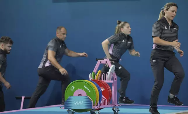 Loaders rush to set the weight on the bar for the next competitor during the women's 59kg weightlifting event at the 2024 Summer Olympics, Thursday, Aug. 8, 2024, in Paris, France. (AP Photo/Kin Cheung)