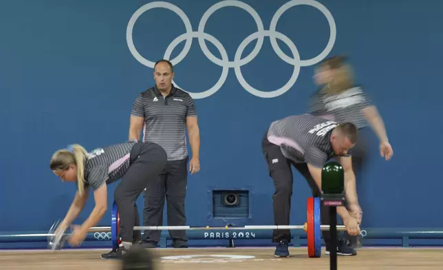 Loaders set the weight on the bar during the women's 59kg weightlifting event at the 2024 Summer Olympics, Thursday, Aug. 8, 2024, in Paris, France. (AP Photo/Kin Cheung)