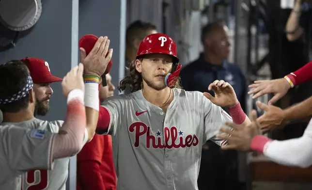 Philadelphia Phillies' Alec Bohm celebrates in the dugout after scoring a run on an RBI single by Nick Castellanos during the sixth inning of a baseball game against the Los Angeles Dodgers in Los Angeles, Tuesday, Aug. 6, 2024. (AP Photo/Kyusung Gong)