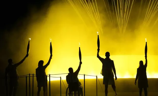 Athletes Charles-Antoine Kouakou, Nantenin Keita, Fabien Lamirault, Alexis Hanquinquant and Elodie Lorandi hold up their torches after lighting the cauldron at the Paralympics Opening Ceremony in Paris, Aug. 28, 2024. (AP Photo/Christophe Ena)