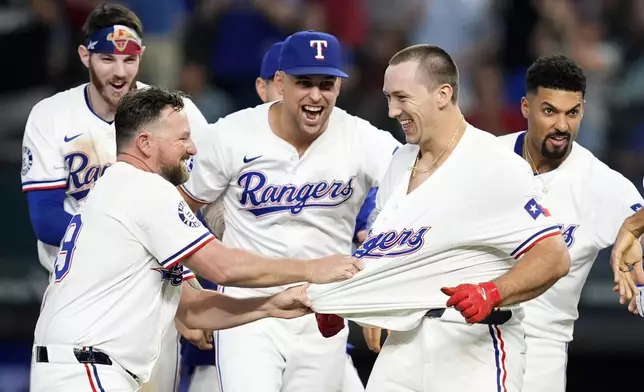 Texas Rangers' Kirby Yates, left, pulls on the jersey of Wyatt Langford, right, as Jonah Heim, left rear, Nathaniel Lowe, center, Marcus Semien, right rear, and the rest of the team celebrate Langford's run-scoring single in the ninth inning of a baseball game against the Pittsburgh Pirates, Wednesday, Aug. 21, 2024, in Arlington, Texas. (AP Photo/Tony Gutierrez)