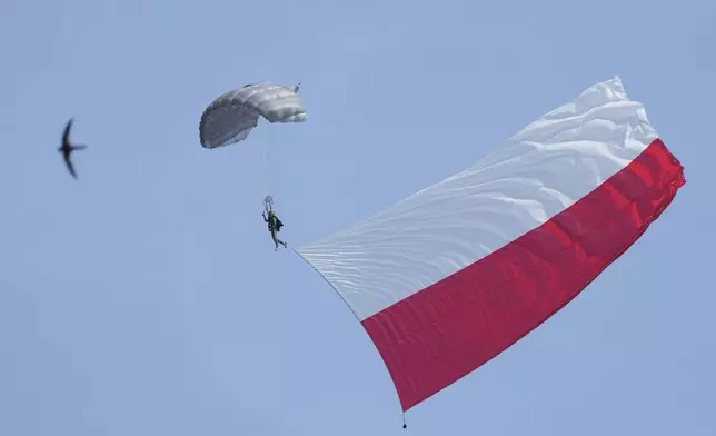 A Polish parachute trooper with a giant Polish flag soars over a military parade during the annual observances on Poland's armed forces day, in Warsaw, Poland, on Thursday, Aug. 15, 2024. (AP Photo/Czarek Sokolowski)