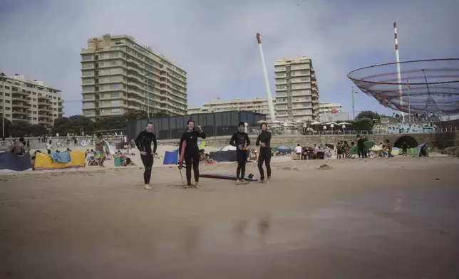 Surf Church members, from left, Zakharii Yarovyi, Lydia Fleete, Ian Carsoso and Lais Cardoso, cheer on their pastor, the Rev. Samuel Cianelli, as he catches a wave in Matosinhos beach in the suburbs of Porto, Portugal on Sunday, Aug. 18, 2024. (AP Photo/Luis Andres Henao)