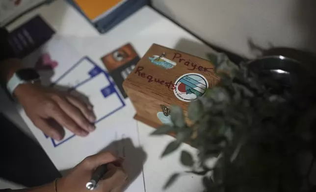 A Surf Church member writes next to a prayer petition box at the church in the suburbs of Porto, Portugal on Sunday, Aug. 18, 2024. (AP Photo/Luis Andres Henao)