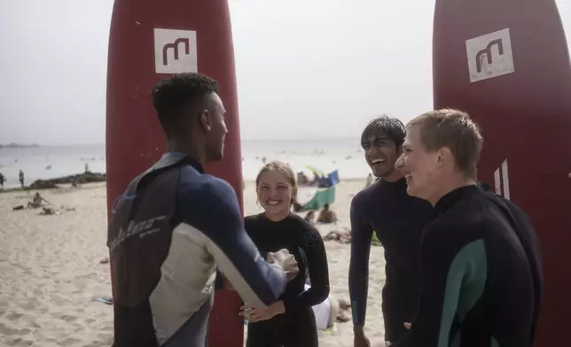 Uliana Yarova, center, laughs while on a break from surfing with other members of Surf Church Church in Matosinhos beach in the suburbs of Porto, Portugal on Sunday, Aug. 18, 2024. The Ukrainian teenager fled her war-torn country with her family after Russia's invasion and found refuge in Porto and Surf Church. (AP Photo/Luis Andres Henao)