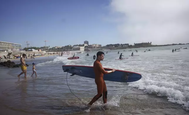 Surf Church's pastor, the Rev. Samuel Cianelli, walks into the Atlantic Ocean to surf with his congregation in Matosinhos beach in the suburbs of Porto, Portugal on Sunday, Aug. 18, 2024. (AP Photo/Luis Andres Henao)