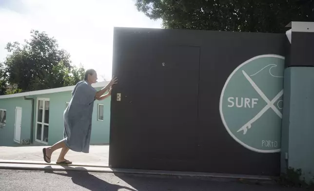 Surf Church member Marielle Louw, from South Africa, opens the garage door to her church after surfing in the suburbs of Porto, Portugal on Sunday, Aug. 18, 2024. (AP Photo/Luis Andres Henao)