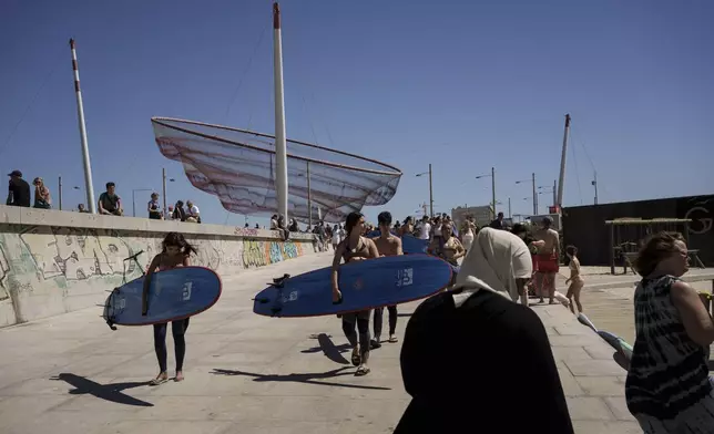 Surf Church members Lais Cardoso, center, and her brother, Ian Cardoso, behind her, carry their surfboards before they catch waves and worship at Matosinhos beach in the suburbs of Porto, Portugal on Sunday, Aug. 18, 2024. (AP Photo/Luis Andres Henao)