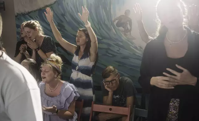 Marielle Louw, raised hands, and Andries Louw, missionaries from South Africa, pray during a worship service at Surf Church in Matosinhos beach in the suburbs of Porto, Portugal on Sunday, Aug. 18, 2024. (AP Photo/Luis Andres Henao)