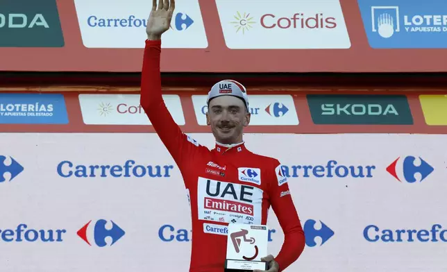 Brandon McNulty, of the United States, wearing the overall leader red jersey, gestures on the podium after winning the first stage of the tour of Spain, La Vuelta, cycling race, an individual time trial with start in Lisbon and finish in Oeiras, Portugal, Saturday, Aug. 17, 2024. (AP Photo/Pedro Rocha)