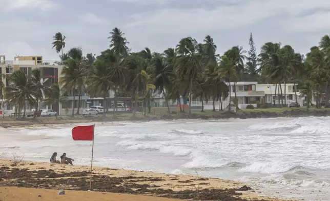 Tourists sit on La Pared beach as Tropical Storm Ernesto passes by Luquillo, Puerto Rico, Tuesday, Aug. 13, 2024. (AP Photo/Alejandro Granadillo)