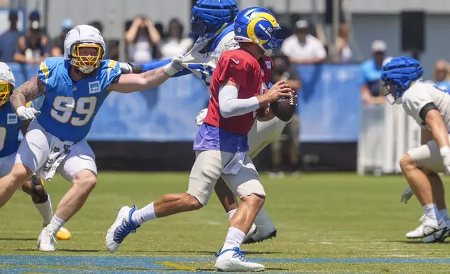 Los Angeles Rams quarterback Matthew Stafford, center front, runs with the ball during NFL football practice at The Bolt in El Segundo, Calif., Sunday, Aug. 4, 2024. Los Angeles Chargers defensive tackle Scott Matlock (99) defends. The Rams and the Chargers are having joint practices. (AP Photo/Damian Dovarganes)