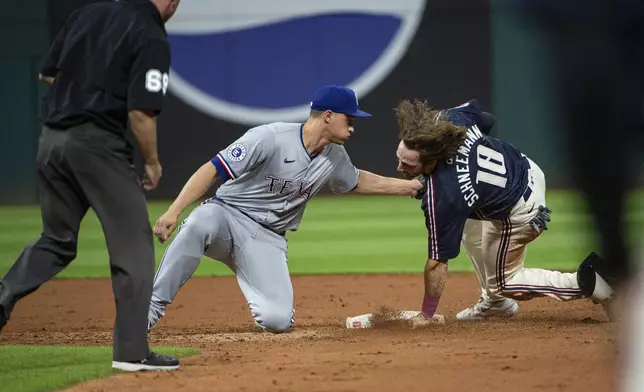 Texas Rangers' Corey Seager, center, is late with the tag as Cleveland Guardians' Daniel Schneemann (18) steals second base with umpire Tom Hannahan, left, watching the play during the fifth inning of a baseball game in Cleveland, Friday, Aug. 23, 2024. (AP Photo/Phil Long)