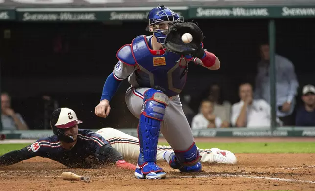 Texas Rangers' Jonah Heim, front, waits for the throw as Cleveland Guardians' Andres Gimenez, rear, slides safely into home plate during the fourth inning of a baseball game in Cleveland, Friday, Aug. 23, 2024. (AP Photo/Phil Long)