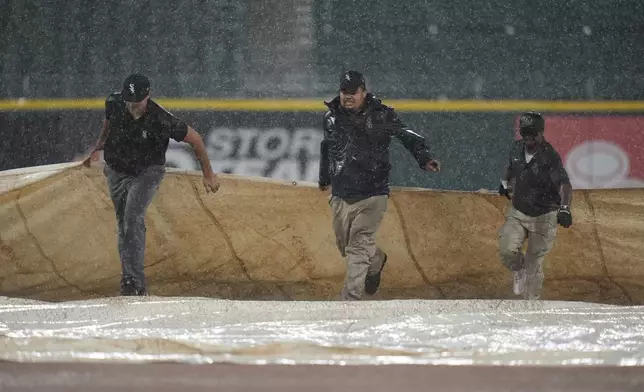 The ground crew covers the field as rain pours down during the first inning of a baseball game between the Texas Rangers and Chicago White Sox, Tuesday, Aug. 27, 2024, in Chicago. (AP Photo/Erin Hooley)