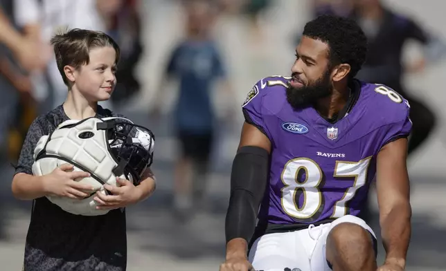 Baltimore Ravens wide receiver Keith Kirkwood (87) rides a bike while a young fan carries his helmet during an NFL football joint training camp practice with the Green Bay Packers Thursday, Aug. 22, 2024, in Green Bay, Wis. (AP Photo/Matt Ludtke)