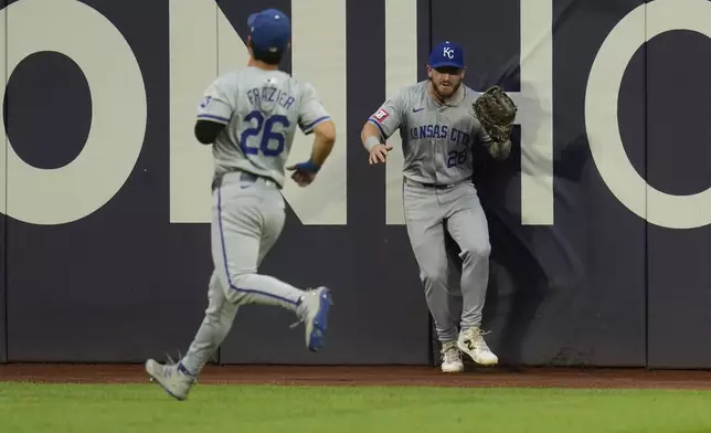 Kansas City Royals center fielder Kyle Isbel (28) crashes into the outfield wall behind teammate Adam Frazier (26) after catching a fly ball hit for an out by Cleveland Guardians' Josh Naylor in the fourth inning of a baseball game Tuesday, Aug. 27, 2024, in Cleveland. (AP Photo/Sue Ogrocki)