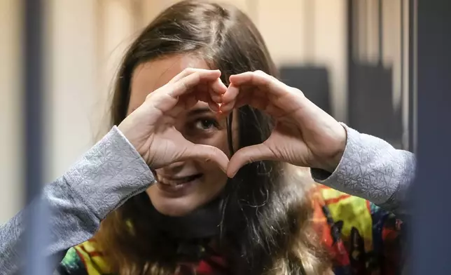 FILE - Sasha Skochilenko, a 33 year-old artist and musician, makes a heart sign while standing behind bars in court in St. Petersburg, Russia, Nov. 13, 2023. (AP Photo/Dmitri Lovetsky, File)