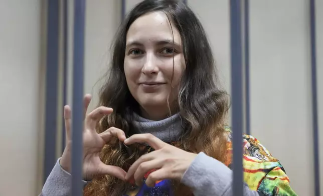 FILE - Sasha Skochilenko, a 33 year-old artist and musician shows a heart behind bars in the court room as she waits for a hearing in the Vasileostrovsky district court in St. Petersburg, Russia, Monday, Nov. 13, 2023. Skochilenko, an artist and musician, was convicted in 2023 of spreading false information about the Russian military and sentenced to seven years in prison. She denied the charges. (AP Photo/Dmitri Lovetsky, Pool, File)