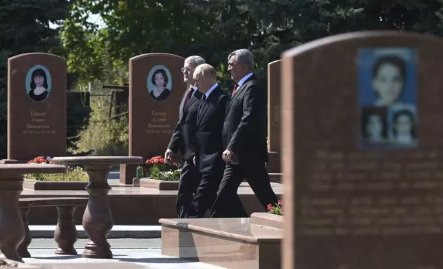 Russian President Vladimir Putin, centre, accompanied by Head of the Republic of North Ossetia-Alania Sergei Menyailo, right, and Presidential Envoy to the North Caucasian Federal District Yury Chaika, attends a ceremony to lay flowers at the City of Angels cemetery, where the victims of the 2004 Beslan school siege were buried, in Beslan, Republic of North Ossetia-Alania, Russia, Tuesday, Aug. 20, 2024. (Vladimir Astapkovich, Sputnik, Kremlin Pool Photo via AP)