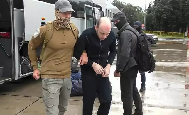 In this image made from video provided by Russian Federal Security Service via RTR on Thursday, Aug. 1, 2024, Germanys Rico Krieger, center, and a Russian Federal Security Service agent, left, leave a bus as they arrive at an airport outside Moscow, Russia. (Russian Federal Security Service/RTR via AP)