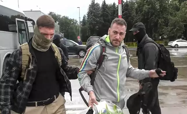 In this image made from video provided by Russian Federal Security Service via RTR on Thursday, Aug. 1, 2024, Germany's Patrick Schoebel, center, is escorted by a Russian Federal Security Service agent, left, as they arrive at an airport outside Moscow, Russia. (Russian Federal Security Service/RTR via AP)