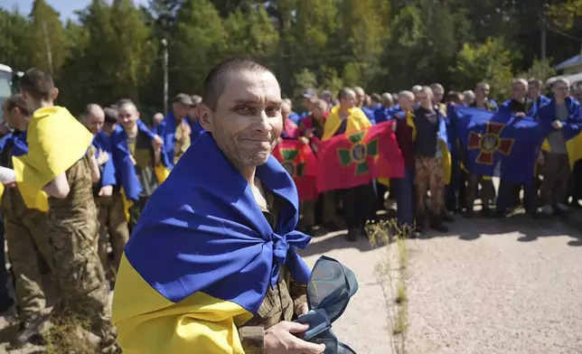 In this photo provided by the Ukrainian Presidential Press Office on Saturday, Aug. 24, 2024, a Ukrainian prisoner of war wrapped in the national flag smiles after a prisoners exchange at an undisclosed location in Ukraine. (Ukrainian Presidential Press Office via AP)