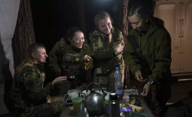 Angelina, second right, a doctor who volunteers at night for an air-defense unit, chats with other members of the unit during their shift near Bucha, Kyiv region, Ukraine, Aug. 9, 2024. (AP Photo/Evgeniy Maloletka)