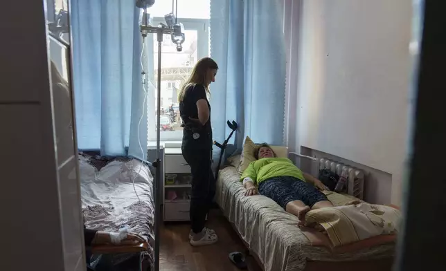 Olena, a doctor who volunteers at night for an air-defense unit, speaks to a patient in a hospital in Bucha, Kyiv region, Ukraine, Aug. 15, 2024. (AP Photo/Vasilisa Stepanenko)