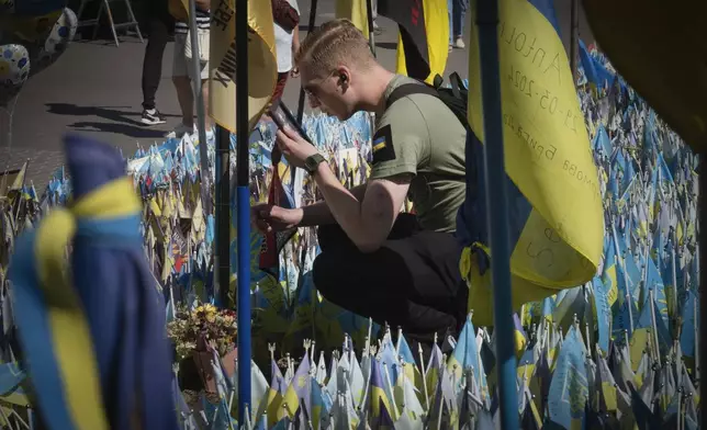 A veteran holds a photo if his comrade at a makeshift memorial for fallen Ukrainian soldiers in Russian-Ukrainian war during Ukrainian Independence Day on Independence Square in Kyiv, Ukraine, Saturday, Aug. 24, 2024. (AP Photo/Efrem Lukatsky)