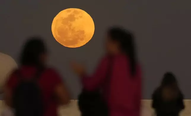 Residents watch the supermoon rise over the "Memorial JK," a monument in honor of the founder of Brasilia, Brazil, Monday, Aug. 19, 2024. (AP Photo/Eraldo Peres)