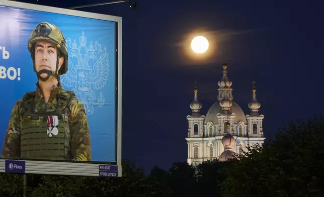 The supermoon is seen over the Smolny Cathedral in St. Petersburg, Russia, Tuesday, Aug. 20, 2024, with an advertising billboard displaying a Russian soldier, participants of the military operation in Ukraine, in the foreground. (AP Photo/Dmitri Lovetsky)